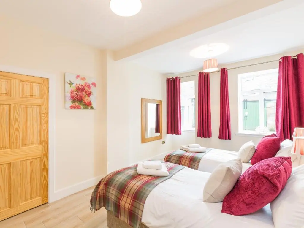 two beds in a bedroom with red curtains at Chauffeur's Cottage with Hot Tub in Cray