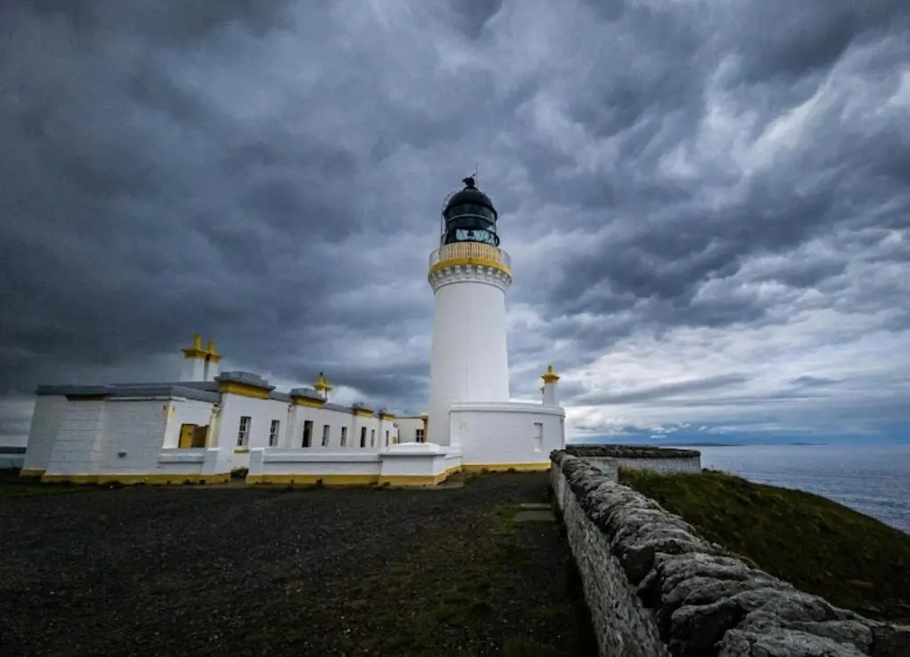 a lighthouse on the side of the ocean with a cloudy sky at Hot Tub Haven Farr North 2 in Wick