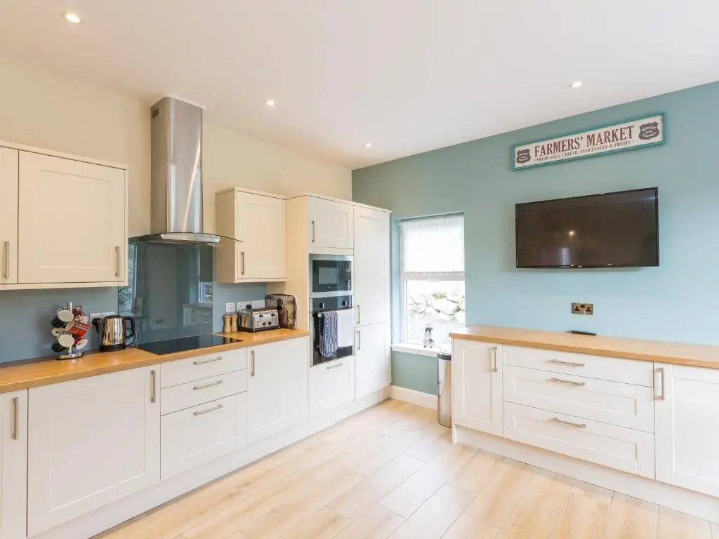 a kitchen with white cabinets and a tv on the wall at Rose Cottage with Hot Tub in Cray