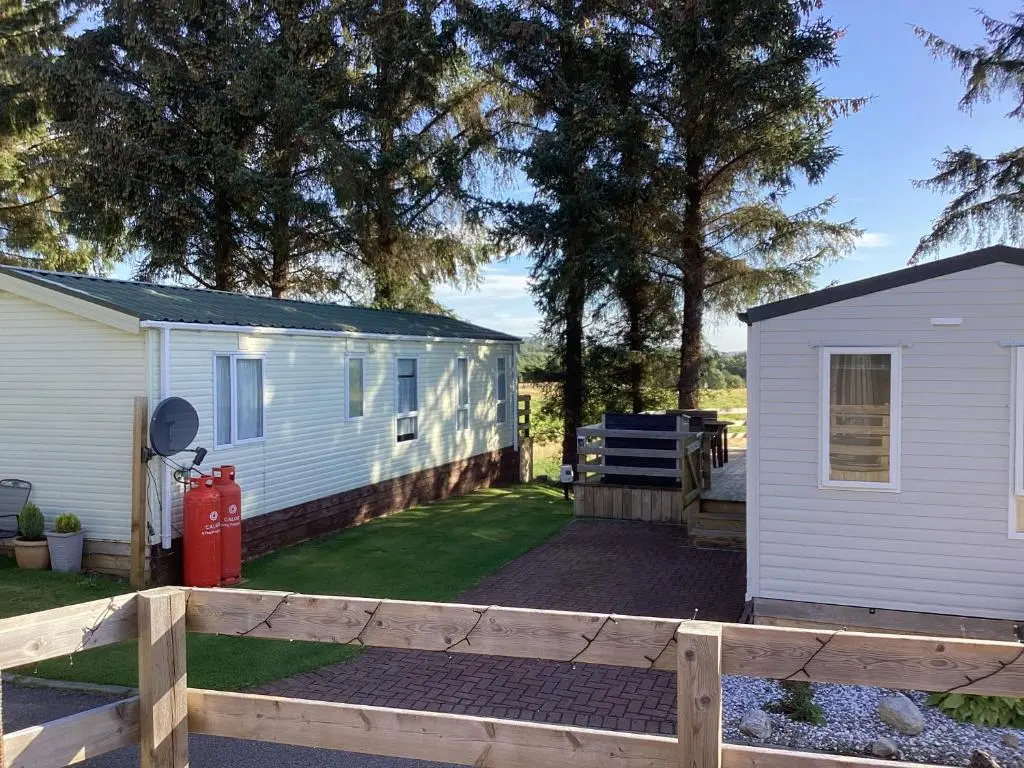a white caravan with a fence and a yard at Dee Lodge in Boat of Garten
