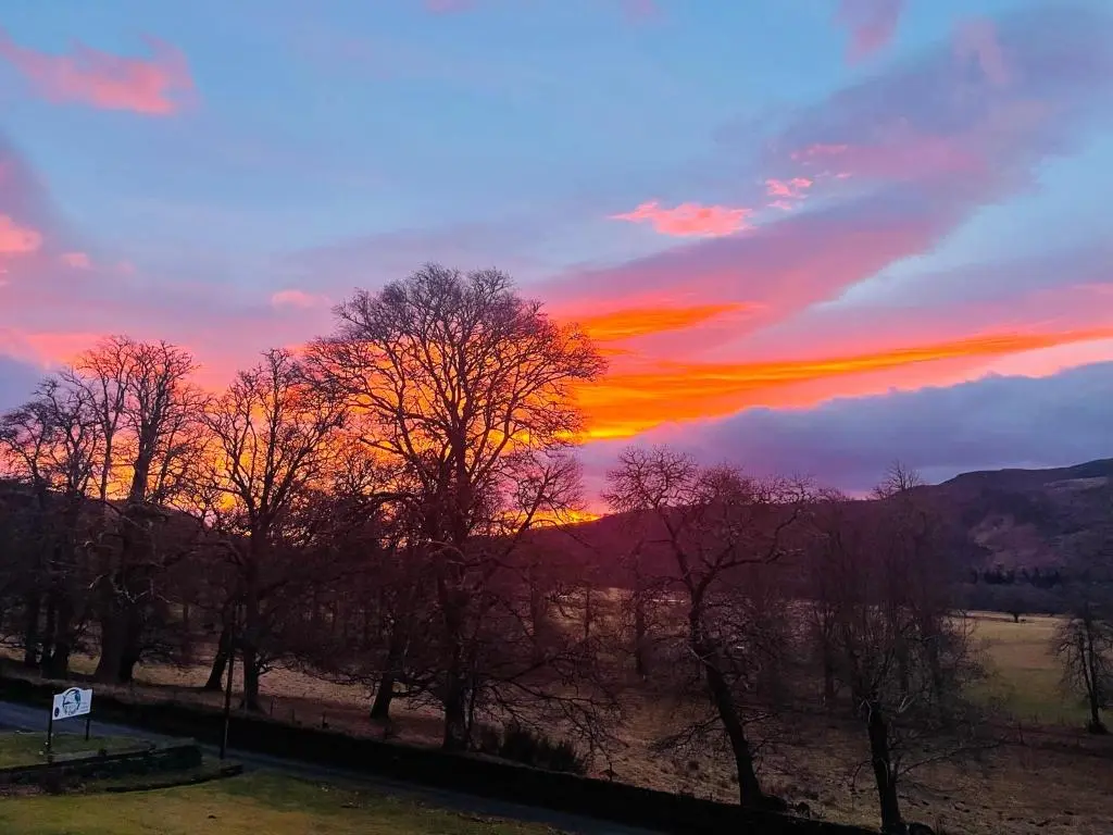 a sunset over a field with trees in the foreground at The Cnoc Hotel in Beauly