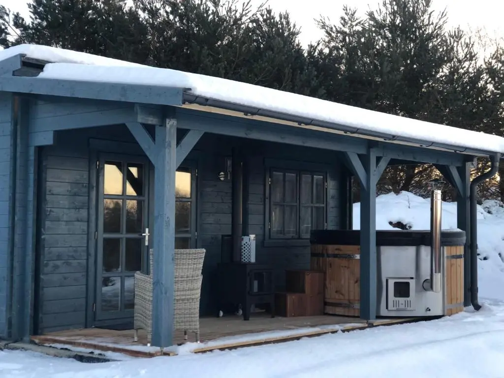 a log cabin with a snow covered roof at Highland cabin - relaxing hot tub in Inverness