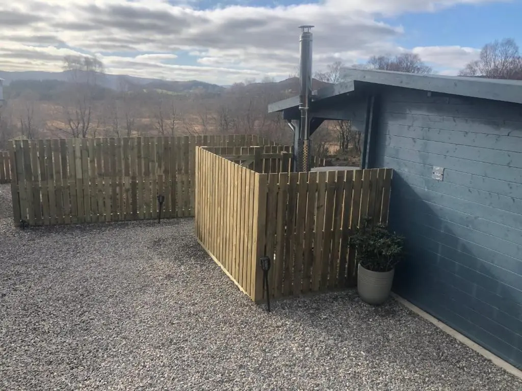 a wooden fence next to a blue building at Highland cabin - relaxing hot tub in Inverness