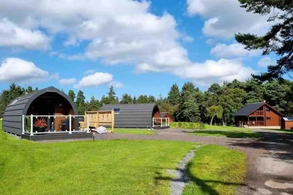 a barn with a yard and a house at Red Squirrel log cabin with hot tub in Keith
