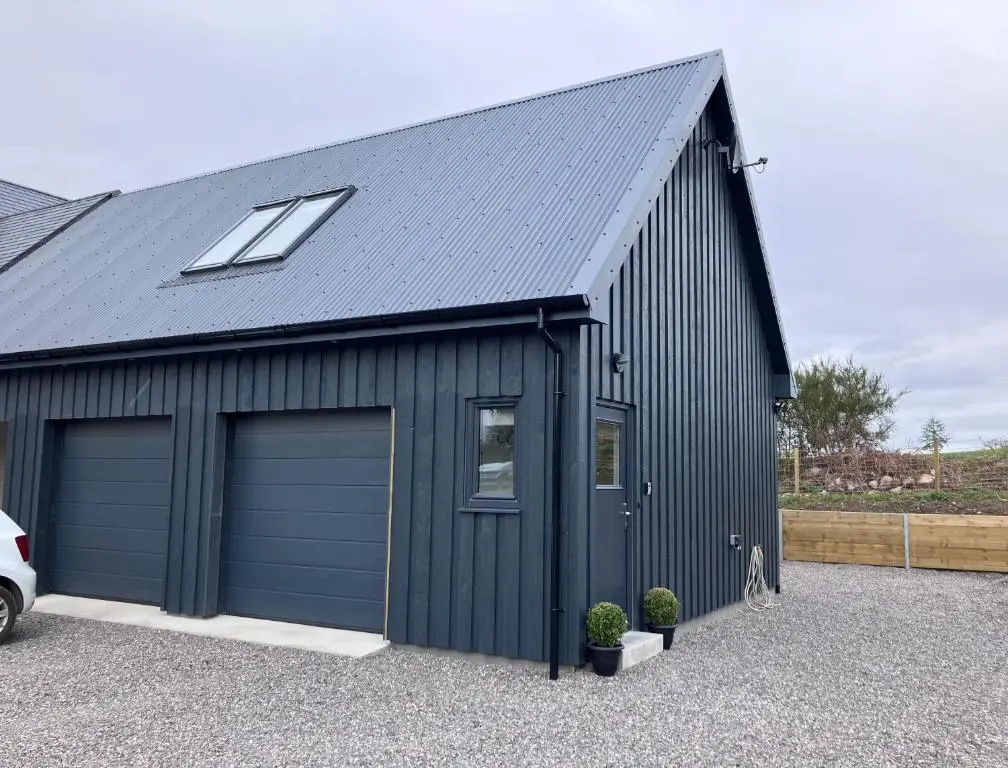 a black garage with two garage doors and a window at Berryfield Holiday Apartment in Inverness
