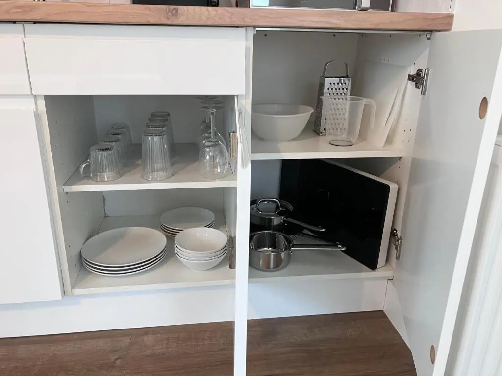a kitchen cabinet with dishes and a microwave at Berryfield Holiday Apartment in Inverness