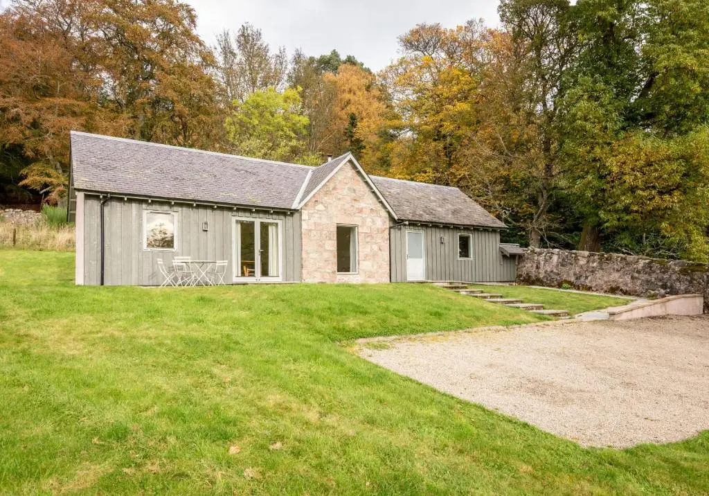 a house with a stone wall next to a yard at The Kennels in Ballogie
