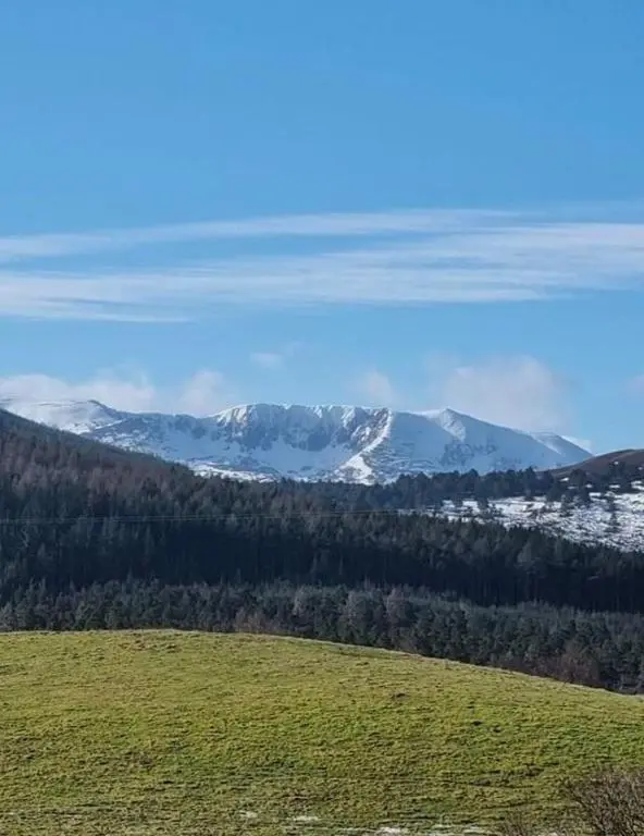a green field with snow capped mountains in the background at Craggan in Ballater