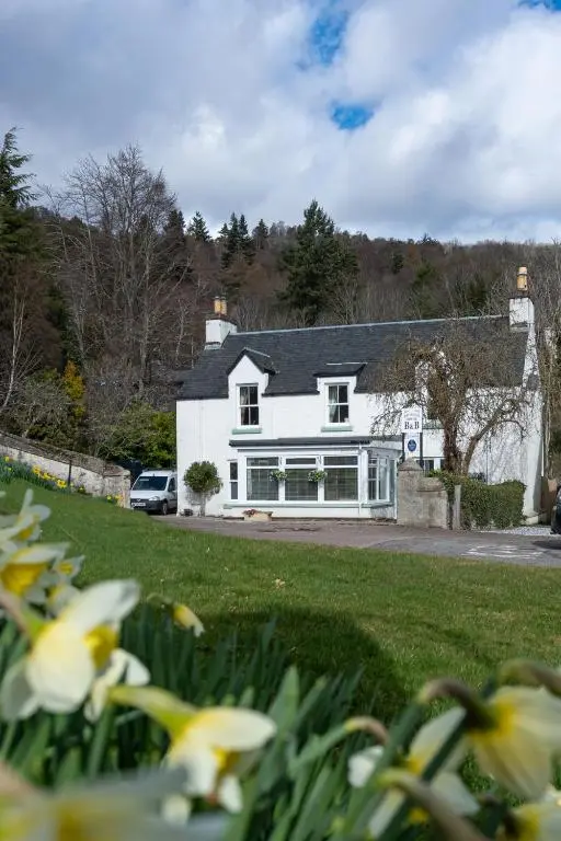 a white house with flowers in front of it at Bridgend House B&B in Drumnadrochit