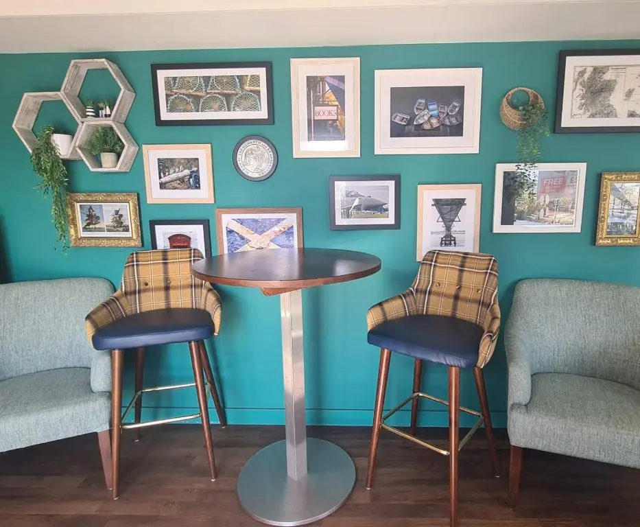 a table and two stools against a wall with pictures at Lyons Retreat in Lossiemouth
