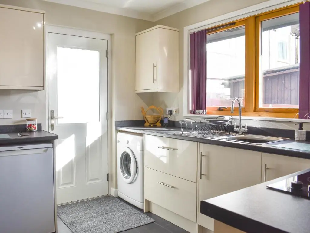a kitchen with white cabinets and a washer and dryer at Cathwill in Newtonmore