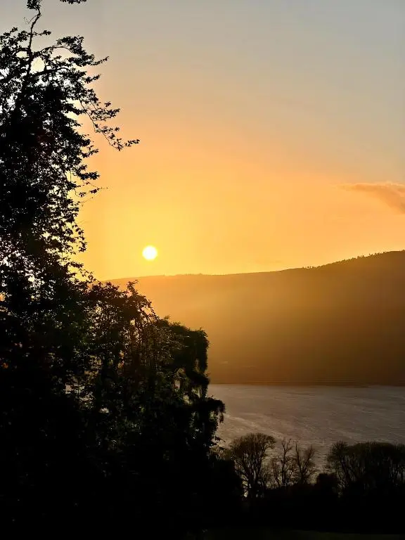 a sunset over the water with a tree at 1 Loch Ness Heights in Inverness