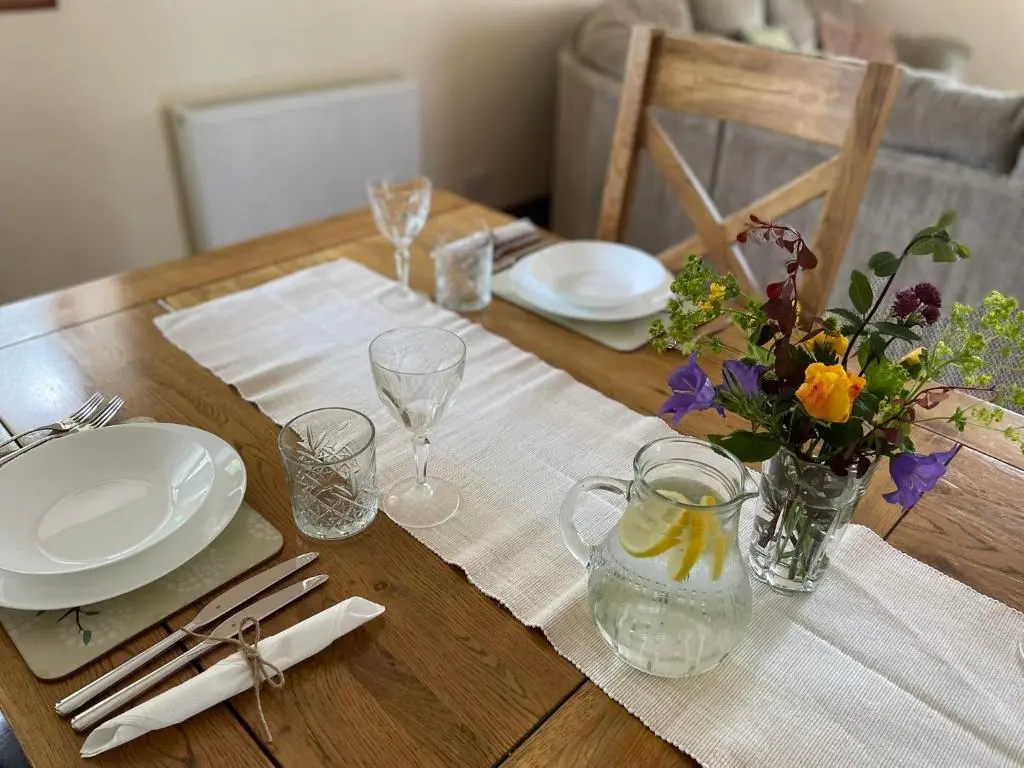 a wooden table with plates and flowers in a vase at Barclay\u2019s But n Ben in Alford