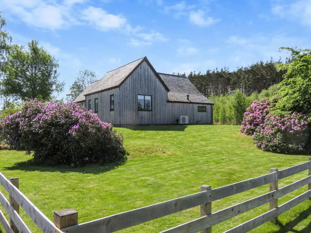 a barn in a yard with a fence and flowers at Old School House in Altnaharra