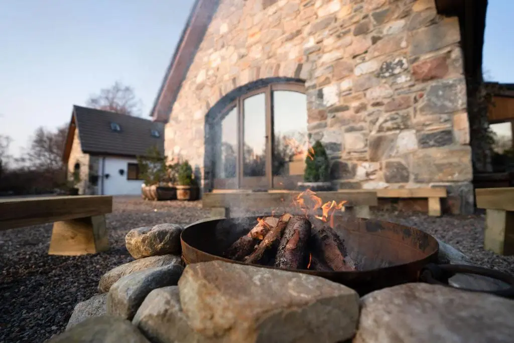 a fire pit in front of a stone building at The Wilds - Seasgair Lodges in Kingussie