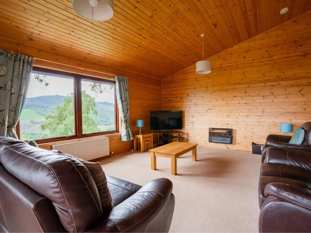 a living room with leather furniture and a large window at Holiday Home Achmony Green by Interhome in Drumnadrochit