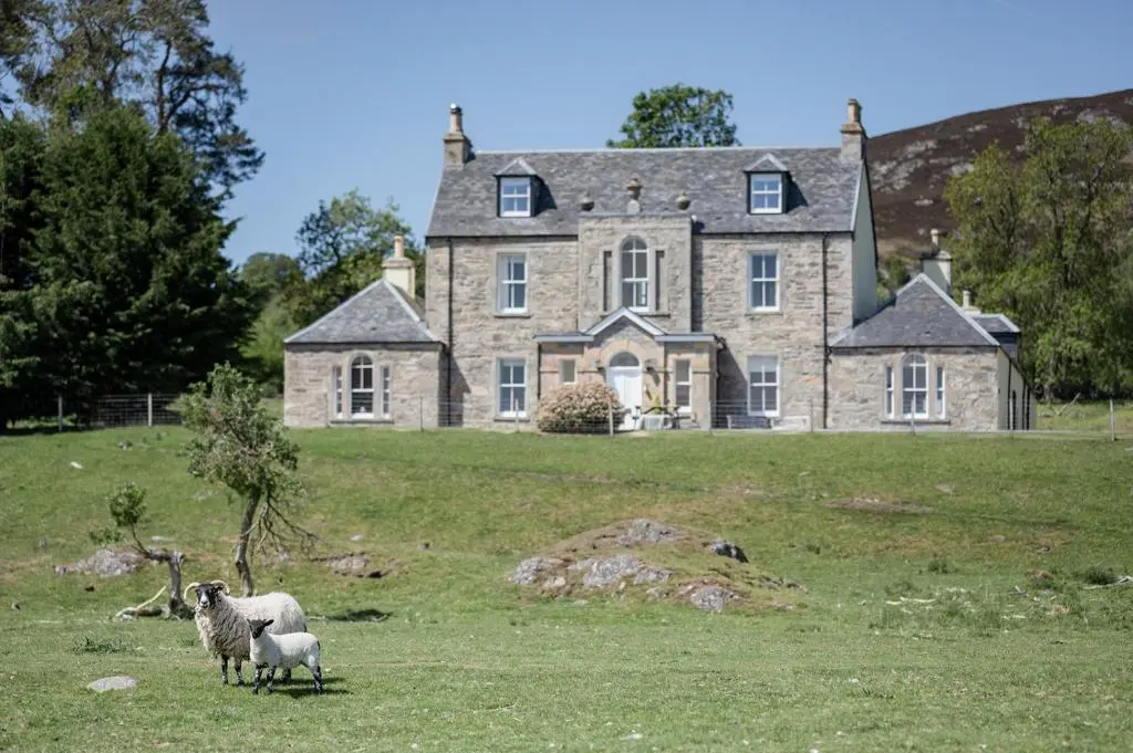 two sheep standing in front of a large stone house at Kincraig House - Seasgair Lodges in Kincraig