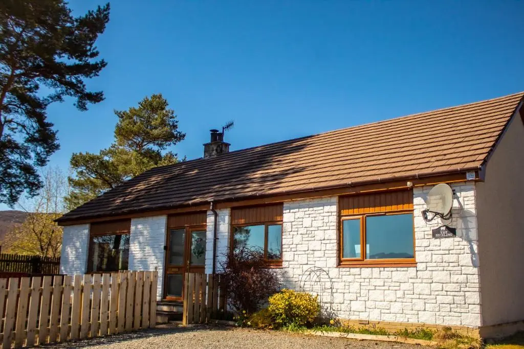a small white brick house with a wooden fence at The Shieling in Aviemore